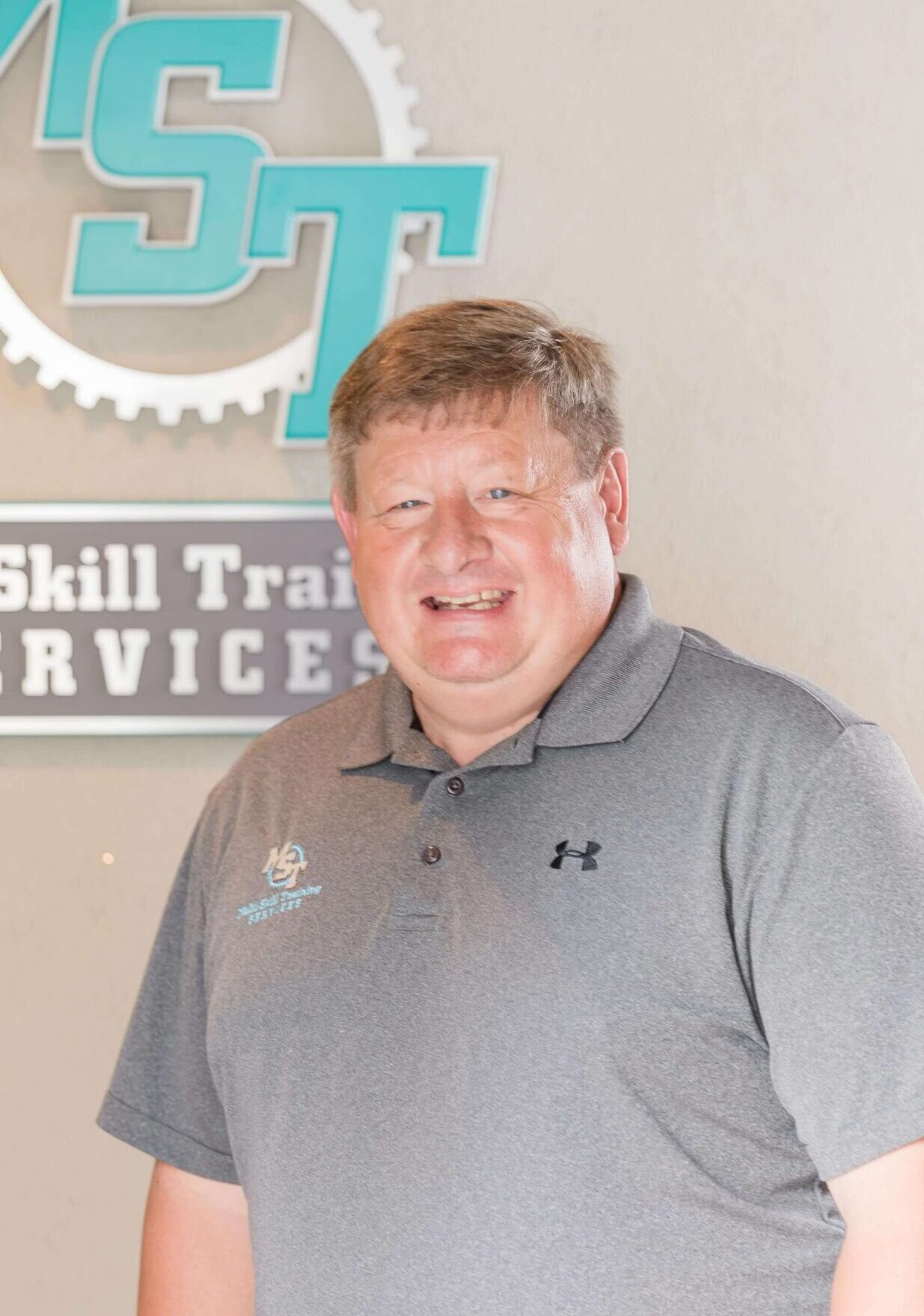 Darin Greifenkamp (VP, Maintenance Excellence) standing next to MST sign on a wall